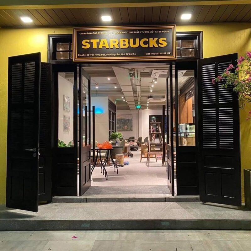 Entrance of Starbucks Hoi An with a wooden sign and black louvered doors on a yellow wall